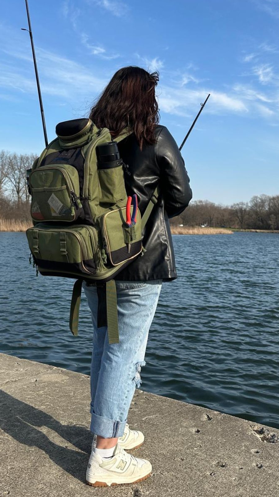 Angler carrying the BassFrontier fishing tackle backpack by the water with rods and pliers in the pockets